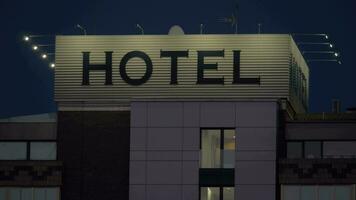 een hotel teken Aan een top van een gebouw tegen donker avond lucht video
