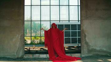 a ásia homem dentro uma vermelho roupão é em pé dentro a velho construção com vidro janelas video