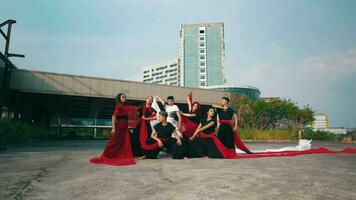 a group of Asian men stood and posed with red veils tied around their bodies in front of a magnificent building video