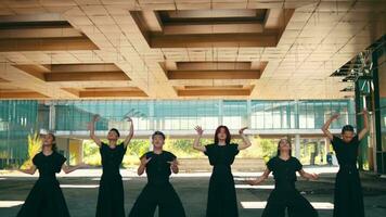 een groep van Aziatisch mannen in zwart kleren dansen met hun handen en vol van enthousiasme onder de gebouw video