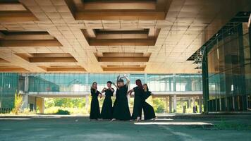 a group of Asian men in black costumes dance a contemporary dance under a patterned building video