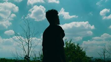 silhouette of an Asian man pensive and thinking against a background full of clouds and a blue sky video