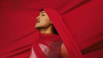 an Asian man bound and strangled by a red cloth with a resigned face in front of a red background video