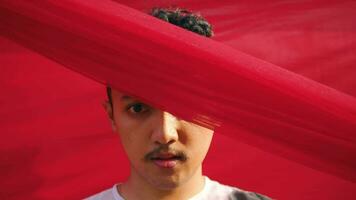 an Asian man with his face and eyes covered by a red veil in front of a red background video