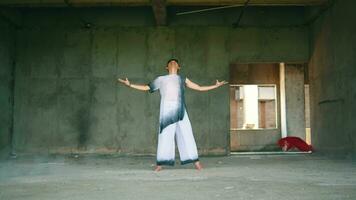 an Asian man unties the cloth on his body while wearing white clothes in an old building video