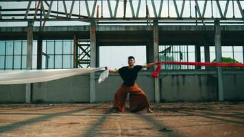 an Asian man bound by white and red cloth with a stressed face in an old building video