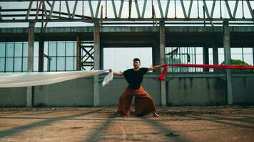 an Asian man bound by white and red cloth with a stressed face in an old building video