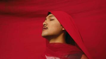 an Asian man bound and strangled by a red cloth with a resigned face in front of a red background video