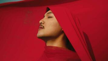 an Asian man bound and strangled by a red cloth with a resigned face in front of a red background video