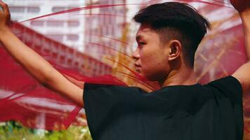 An Asian man holds a red scarf with both hands as the wind blows and blows the cloth away video