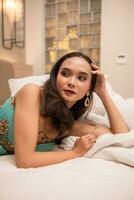 a beautiful Asian woman is relaxing on a white bed while wearing makeup and dress photo