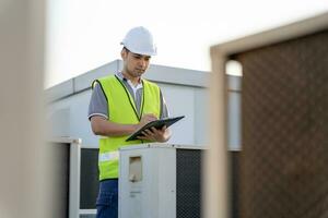 Asian maintenance engineer works on the roof of factory. contractor inspect compressor system and plans installation of air condition systems in construction. Checklist, inspector, control photo