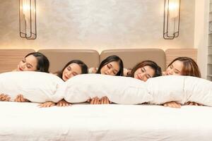 a group of Asian women are sleeping and leaning on white pillows with their friends in a luxury hotel photo
