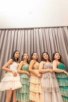 un grupo de asiático mujer son en pie en frente de el cortinas de un lujo hotel mientras vistiendo vestidos a un fiesta foto