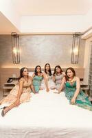 a group of Asian women in beautiful dresses sitting together on a white bed while staying photo