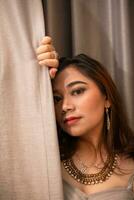 un hermosa asiático mujer participación el cortinas mientras posando para fotos en un estudio
