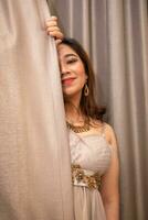 un hermosa asiático mujer participación el cortinas mientras posando para fotos en un estudio