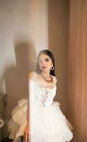 an Asian woman in a white dress and beautiful makeup is sitting elegantly on a white toilet in a luxurious hotel room photo