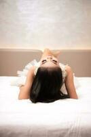 an Asian woman with black hair is sleeping on a white bed in an elegant hotel photo