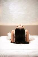 an Asian woman with black hair is sleeping on a white bed in an elegant hotel photo