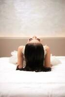 an Asian woman with black hair is sleeping on a white bed in an elegant hotel photo