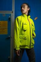 an Asian man in a green jacket is posing in front of a blue door photo