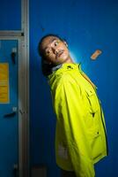 an Asian man in a green jacket is posing in front of a blue door photo