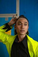 an Asian man with long curly hair is posing in front of a blue wardrobe photo