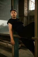 un asiático hombre colgando desde el hierro de un abandonado edificio mientras vistiendo un negro camisa foto