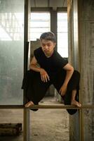 an Asian man hanging from the iron of an abandoned building while wearing a black shirt photo