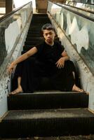 an Asian man in black clothes is sitting in a broken and abandoned elevator in an old building photo