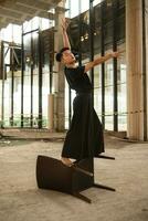 an Asian man is standing on a wooden chair while wearing a black dress in an old building photo