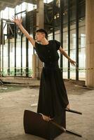 an Asian man is standing on a wooden chair while wearing a black dress in an old building photo