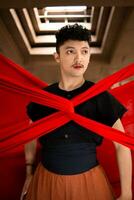 an Asian man stands under the light as his body is bound by a red cloth photo