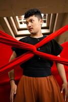 an Asian man stands under the light as his body is bound by a red cloth photo