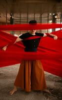 an Asian man standing proudly among the red cloth that dangles in an old building photo