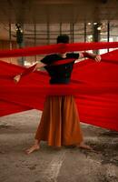 an Asian man standing proudly among the red cloth that dangles in an old building photo