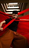 an Asian man in a black shirt is strangled with a red cloth while standing in an old building against a red background photo