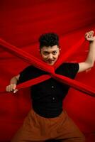 an Asian man stands in front of a red x-shaped cloth and holds it with both hands photo