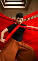 an Asian man in a black shirt is strangled with a red cloth while standing in an old building against a red background photo