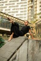 an Asian man sleeps on a marble rock while wearing black clothes around an old building photo