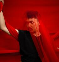 an Asian man in a black shirt covering his face with a red cloth with a frightening facial expression in front photo