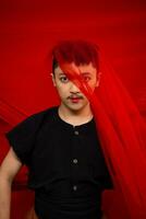 un asiático hombre en pie en frente de un rojo paño con un rojo paño colgando terminado su cabeza foto