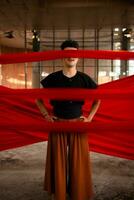 an Asian man stands between a red cloth and blindfolds while in an old building photo