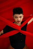 an Asian man stands in front of a red x-shaped cloth and holds it with both hands photo