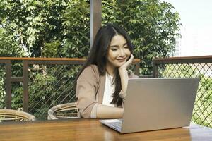 Smiling young Asian woman working remotely from cafe using her laptop, employee getting ready for online video-call interview photo