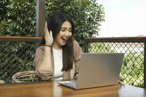 Young Asian woman doing video conference on laptop computer while sitting at the cafe, having meeting photo