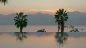 Resort scene at sunset Swimming pool with palms, sea and mountains video