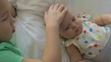 Boy lying on a bed with his baby sister and stroking on her head video