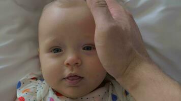 A closeup of a baby girl's face and a father's hand touching her video